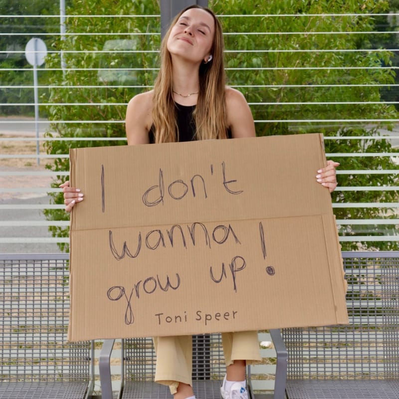 Grow Up cover art — Toni Speer holding a cardboard sign reading “I don’t wanna grow up!”