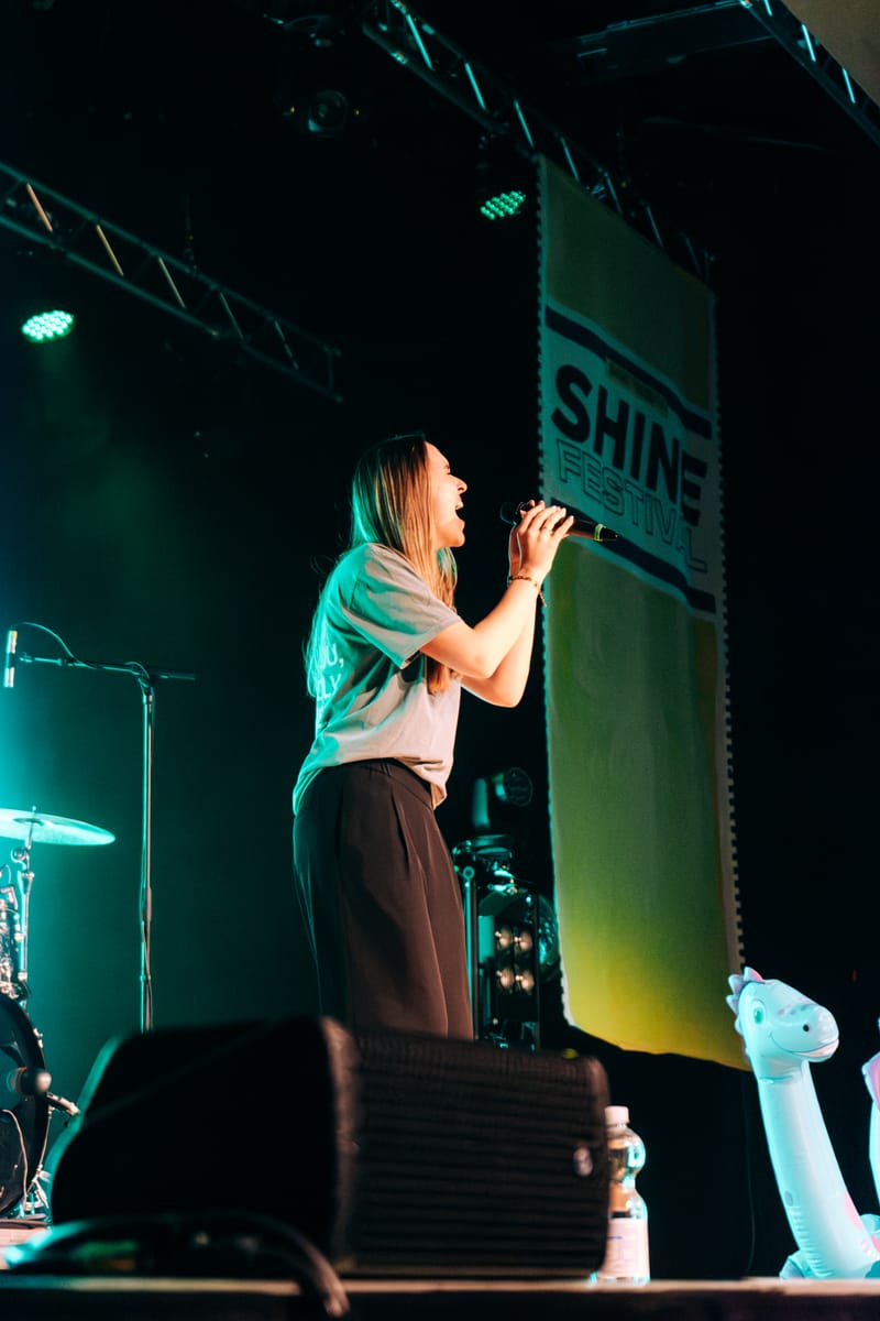 Toni Speer singing into a handheld microphone under teal stage light.